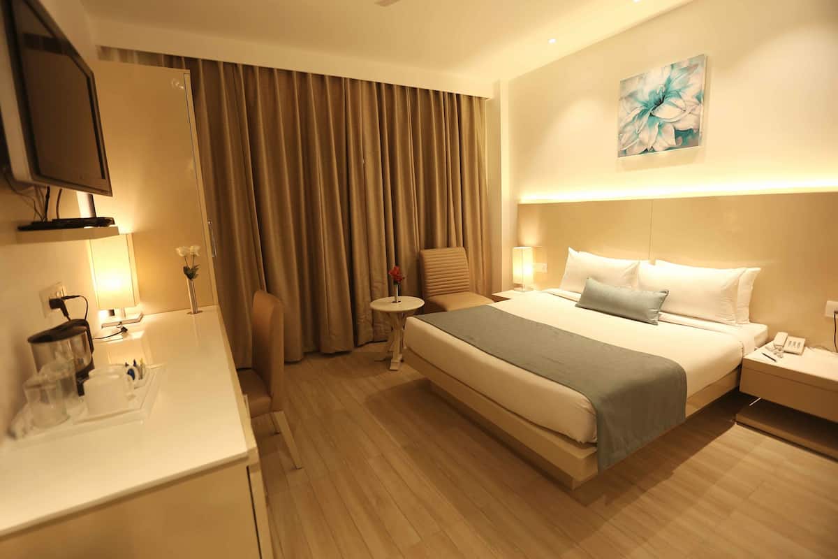 A hotel room with a bed, bedside table, lamp, and a TV mounted on the wall.