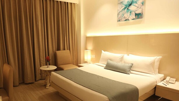 A hotel room with a large bed, a chair, a small table, and a painting on the wall. - Shanti Palace (New Delhi)