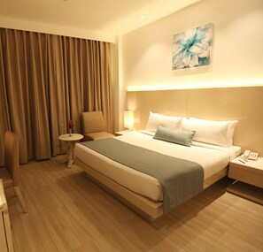 A hotel room with a large bed, a chair, a small table, and a painting on the wall. - Shanti Palace (New Delhi)