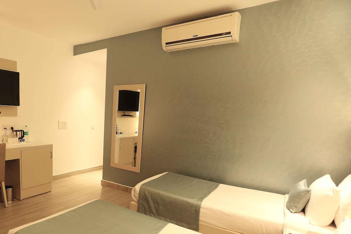 A hotel room with two beds, a desk, a mirror, and an air conditioning unit.
