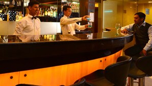 A bar area with a curved counter, bar stools, and a mirrored wall reflecting the bar. - Shanti Palace (New Delhi)