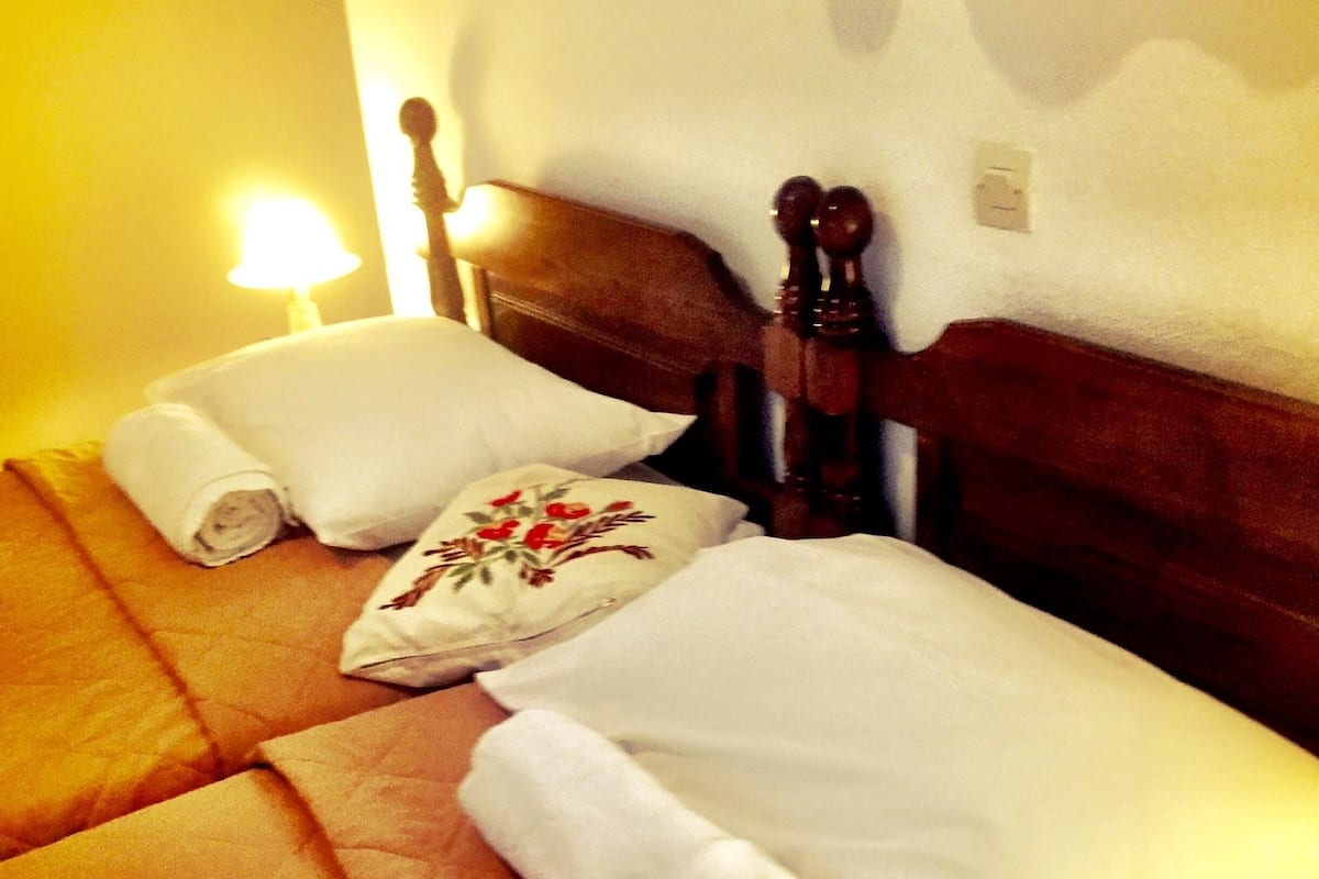 A hotel room with two beds, each with a rolled white towel and a pillow with floral embroidery.