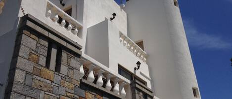 A building with a stone facade and white walls, featuring balconies with white railings and black lantern-style lights.