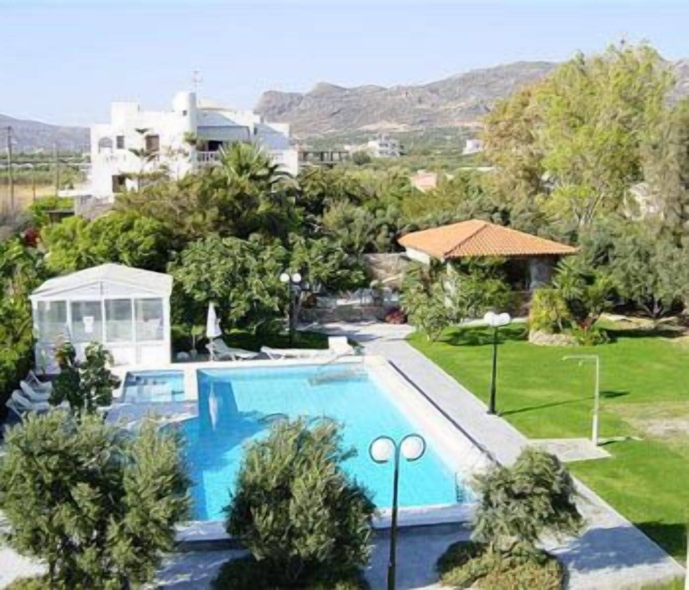 A swimming pool with a glass enclosure, surrounded by greenery and a white building with a dome roof in the background.