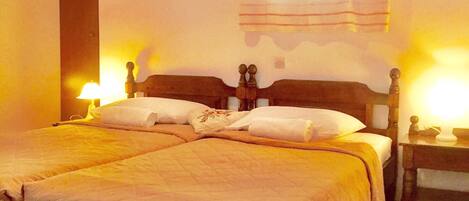 Una cama doble con cabecera de madera, dos mesitas de noche y un ventanal con cortinas.