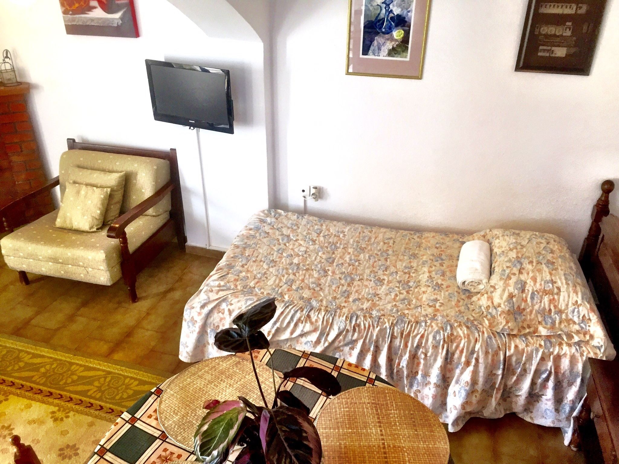 A bedroom with a bed, a chair, a television, and a wall-mounted TV.
