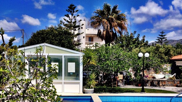 A swimming pool with clear blue water, surrounded by greenery and a small glass-walled structure. - Irene Villas (Ierapetra)