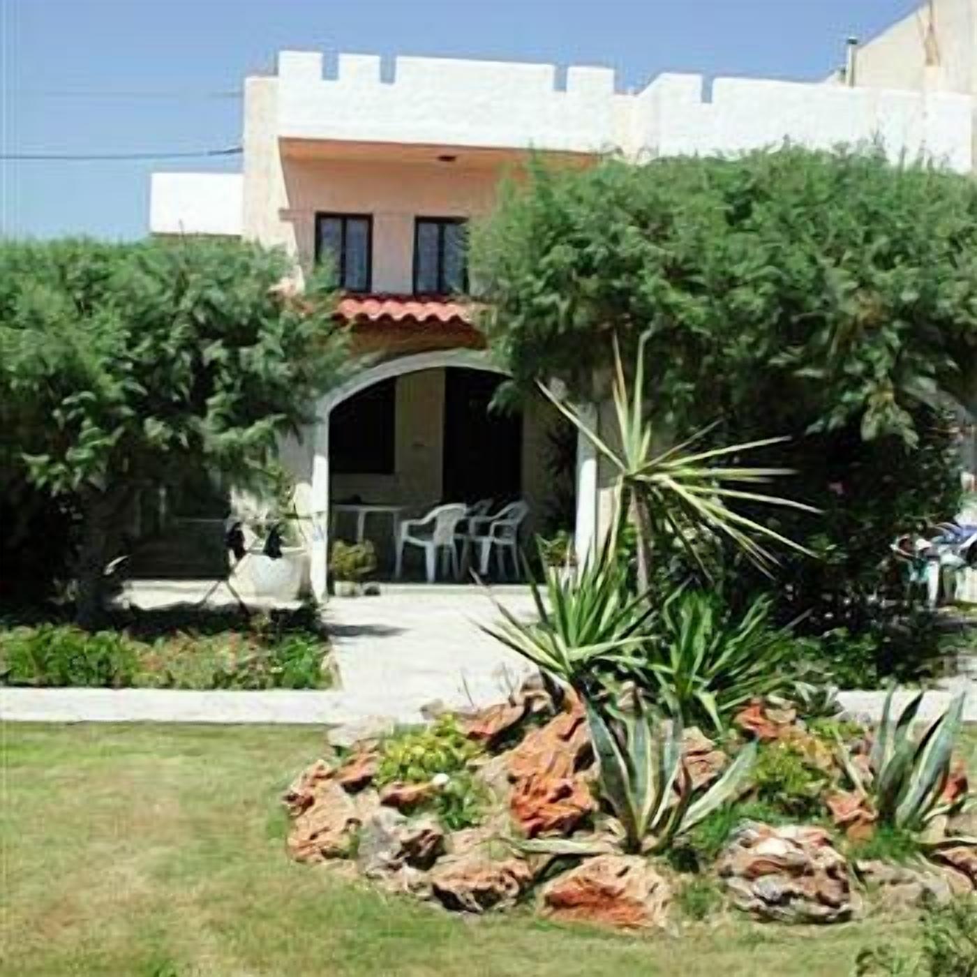 Un edificio con fachada blanca y tejado de tejas rojas, rodeado de un jardín con rocas y plantas.