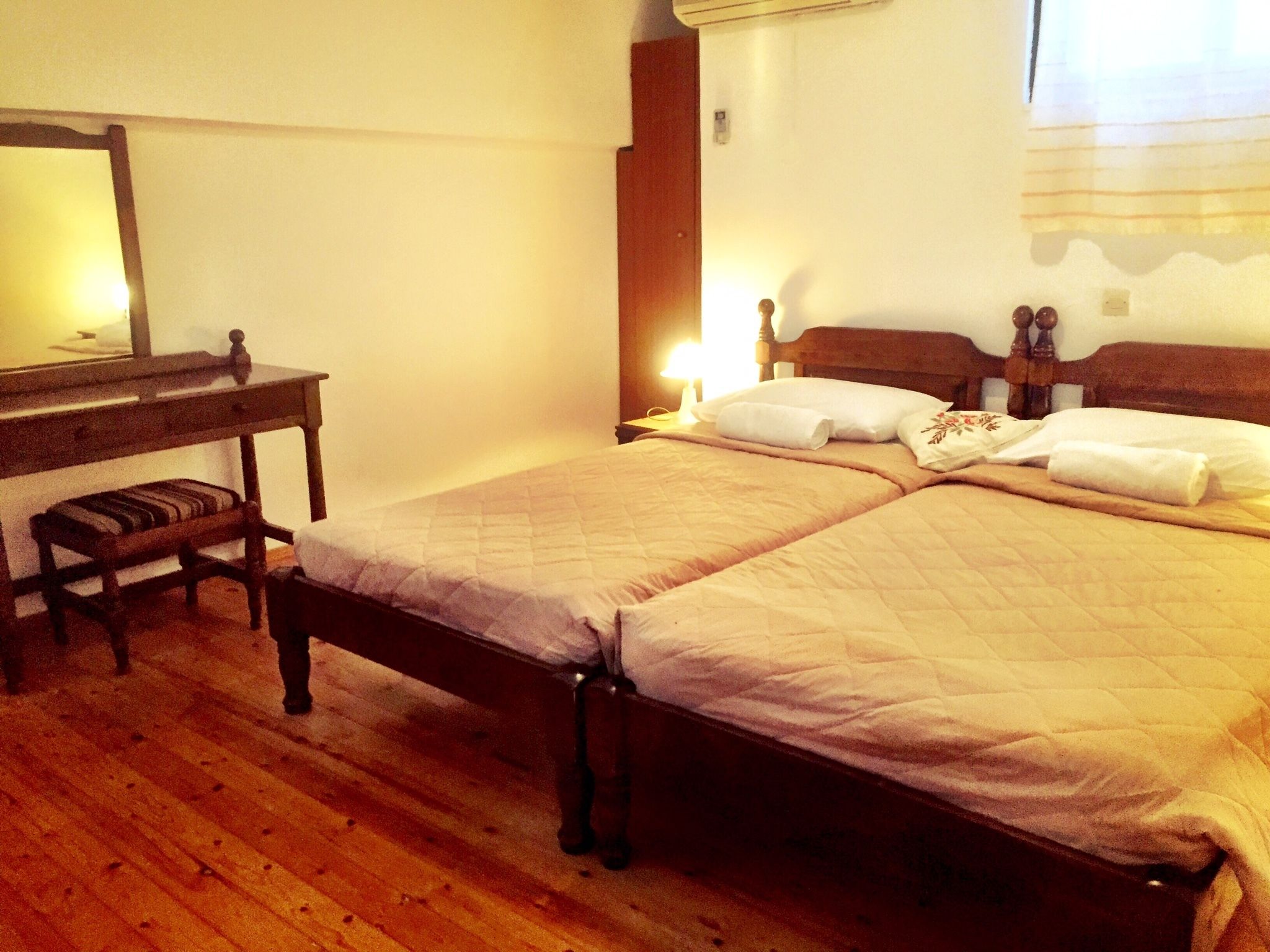 Una cama doble con cabecera de madera, una mesita de noche con lámpara y un banco.