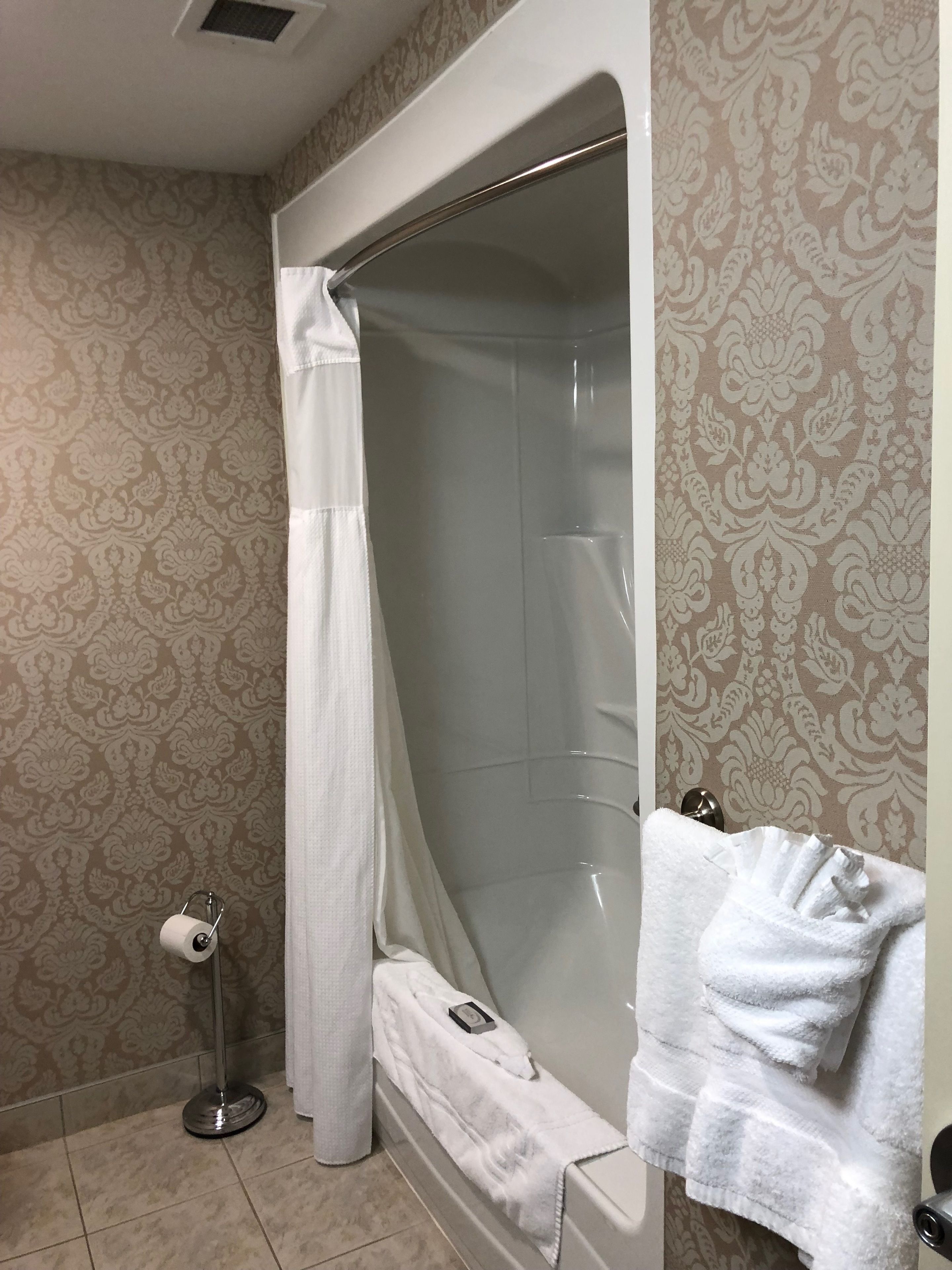 A bathroom with a bathtub, a shower curtain, a towel rack, and a toilet paper holder.