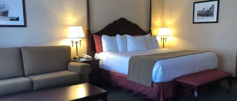 A hotel room with a bed, a sofa, a nightstand, a lamp, and a picture on the wall.