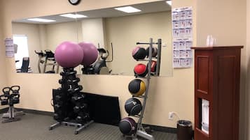 Un gimnasio con equipo de ejercicio, un reloj y carteles instructivos en la pared.
