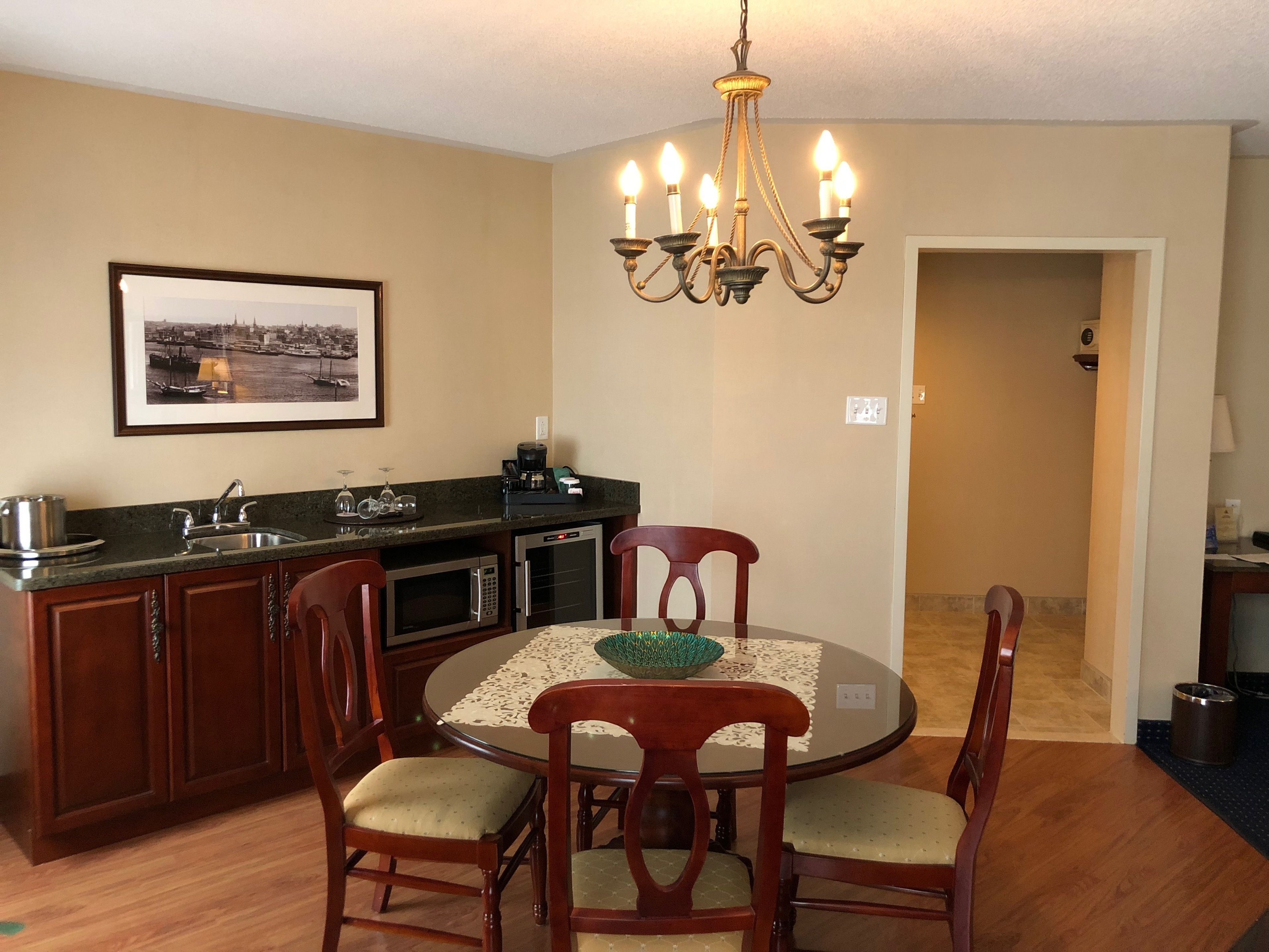 A compact kitchen with a dining area, featuring a chandelier, a framed cityscape, and a small refrigerator.