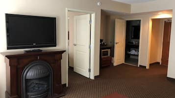 A hotel room with a flat-screen TV mounted above a fireplace, a wooden bench, and a carpeted floor.