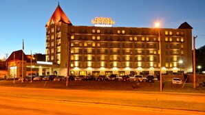 Un hotel gran amb múltiples pisos i una torre destacada, amb una façana ben il·luminada i un pàrquing amb diversos cotxes.