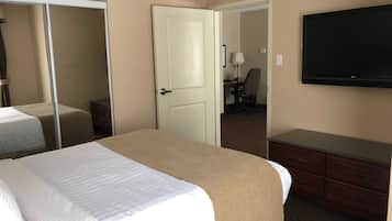 A hotel room with a bed, a dresser, a TV, and a door leading to another room.