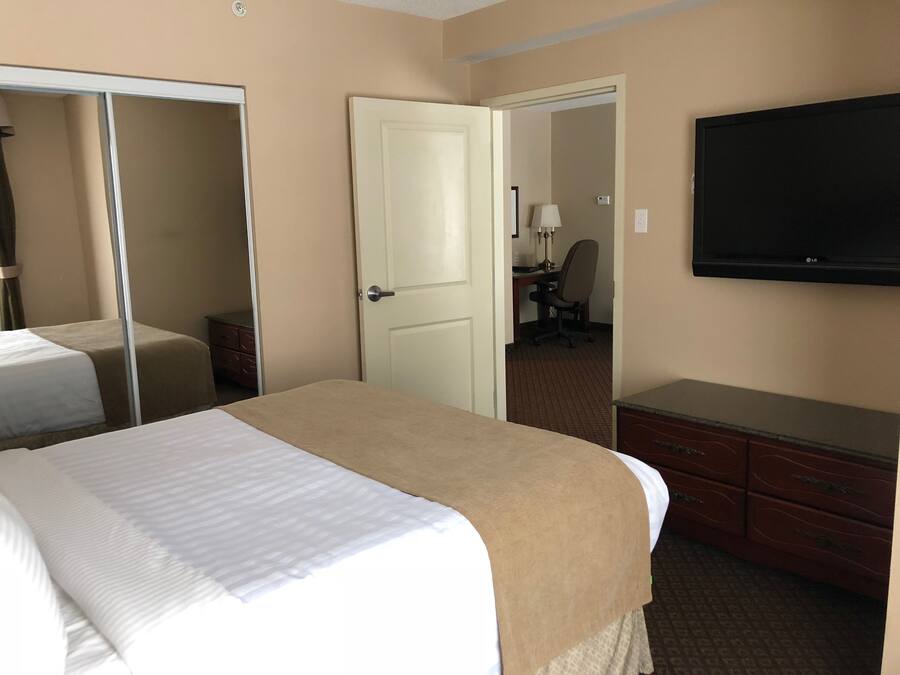 A hotel room with a bed, a dresser, a TV, and a door leading to another room.