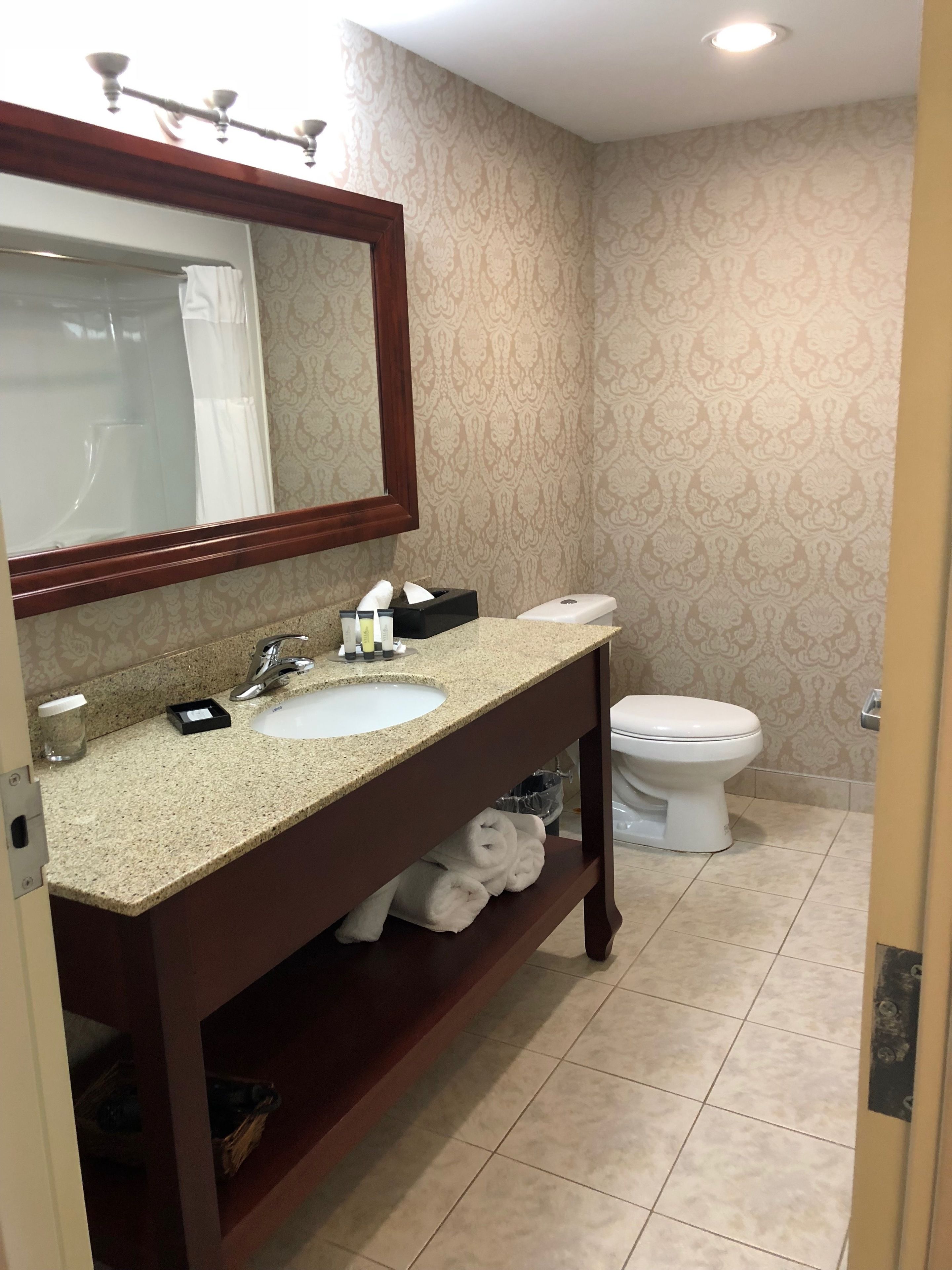 Un baño con lavamanos, espejo, toallero y retrete.