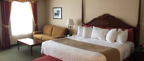 A hotel room with a large bed, a sofa, a desk, and a bench.