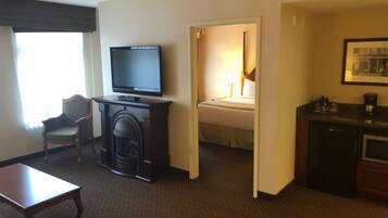 A hotel room with a television, a fireplace, a bed, a desk, and a kitchenette.