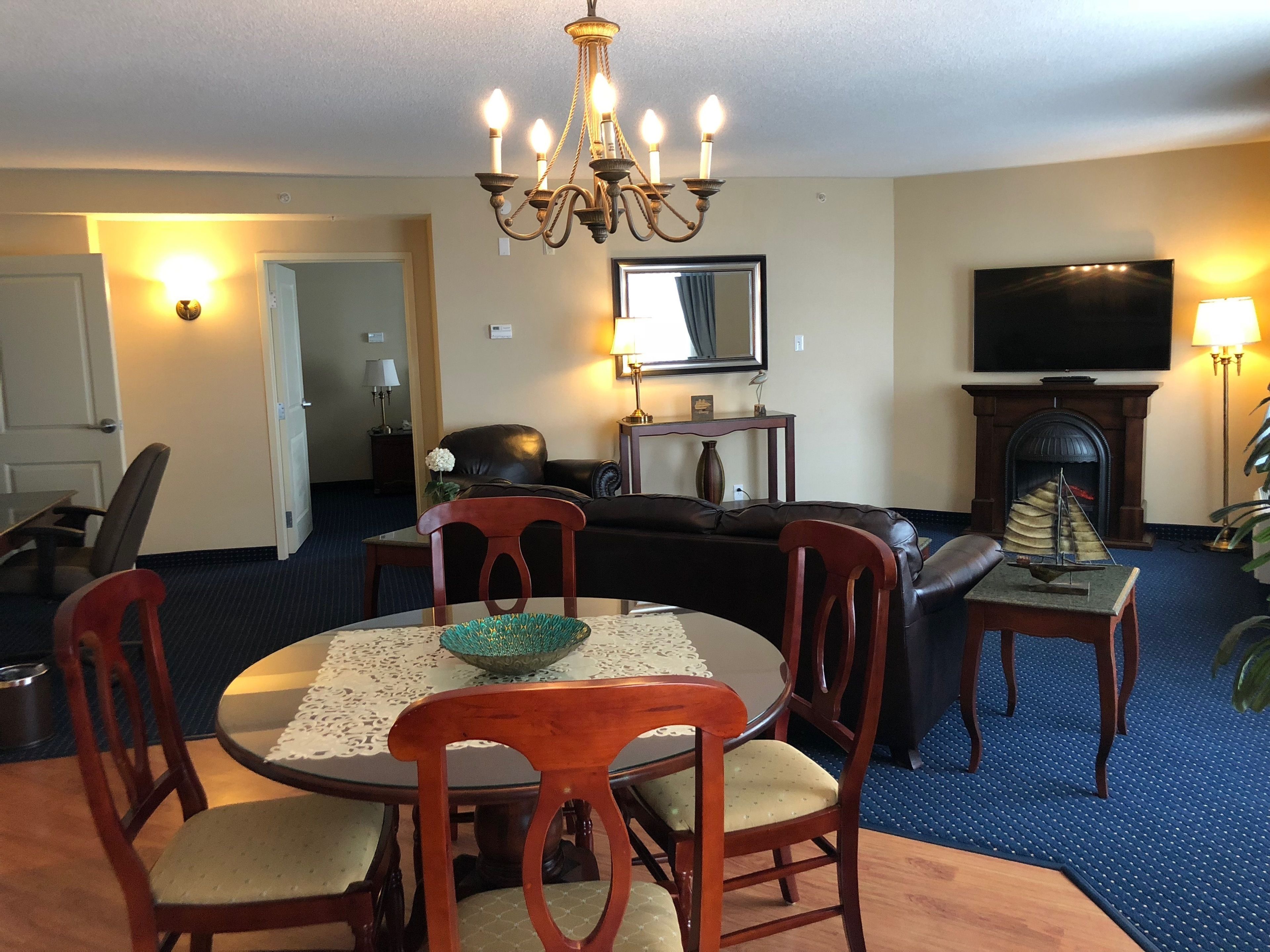A living room with a chandelier, a fireplace, a television, and a dining area with chairs and a table.