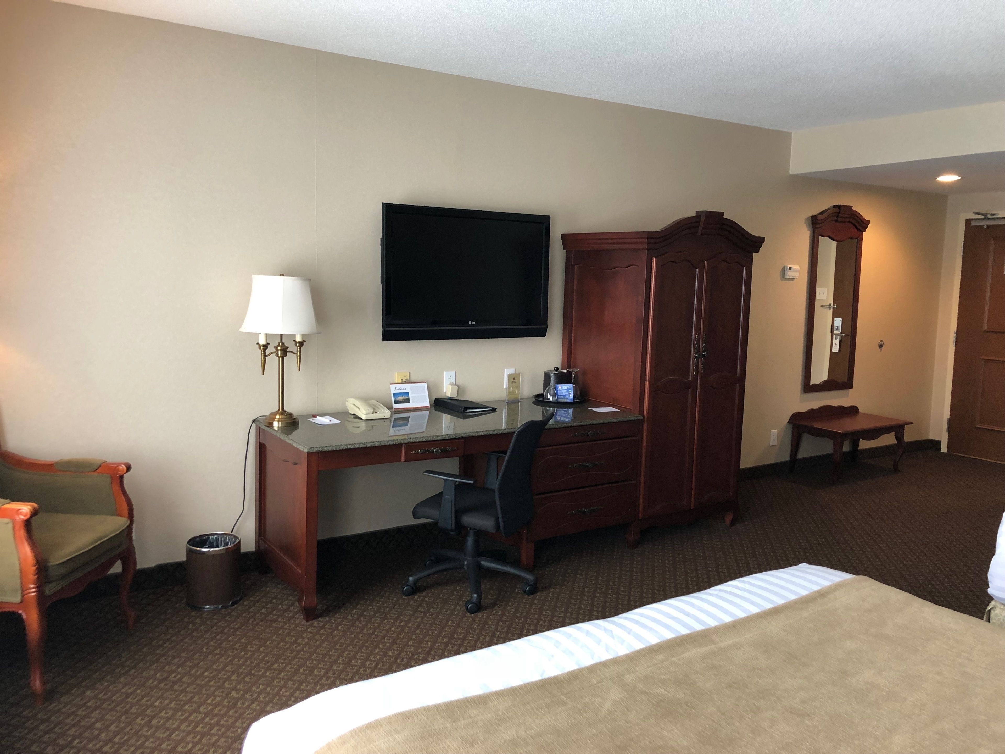 Une chambre d’hôtel comprenant un lit, un bureau, une chaise, une télévision, une armoire et une petite table avec une lampe.