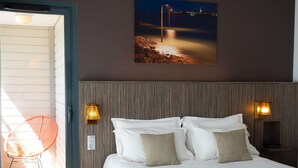 Une chambre d’hôtel avec un lit, deux lampes fixées au mur, un tableau représentant une vue nocturne et une chaise près de la porte.