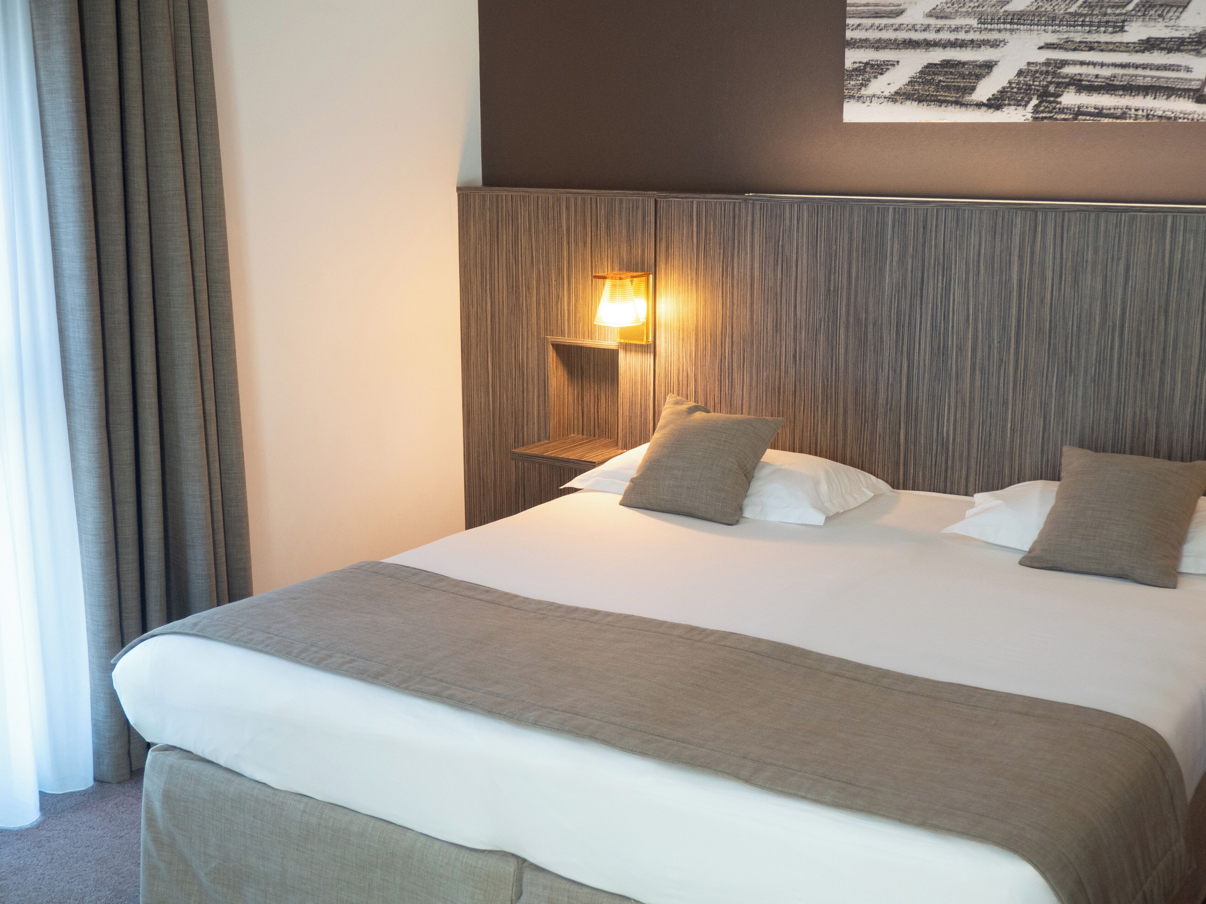 A hotel room with a large bed, a nightstand with a lamp, and a wall-mounted artwork.