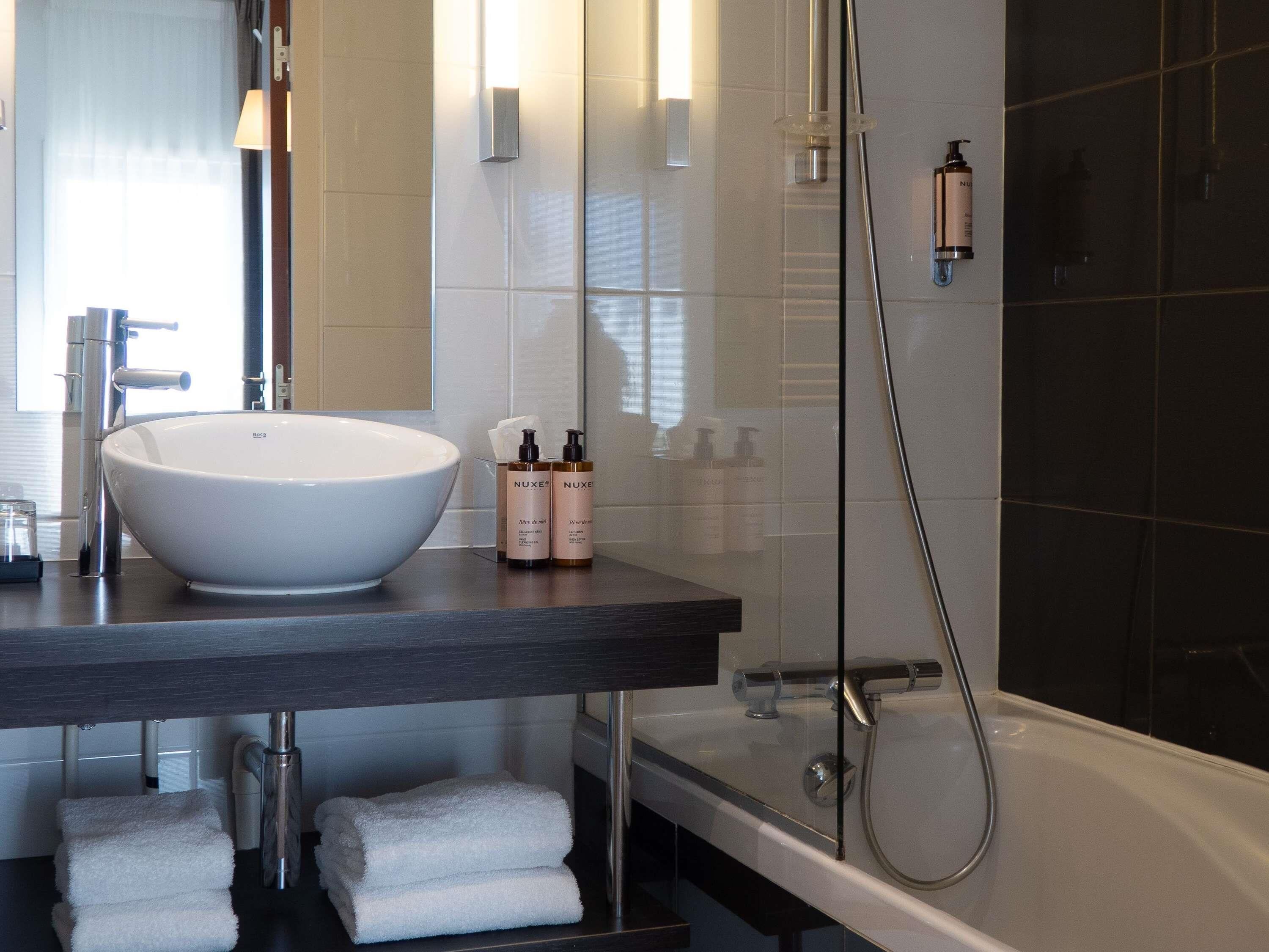 Een moderne badkamer met een groot wit wastafelmeubel, een donker aanrechtblad, een glazen douchecabine en netjes opgevouwen witte handdoeken.