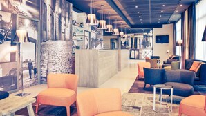 Un hall d’hôtel moderne, doté d’espaces aménagés avec des sièges, d’un comptoir d’accueil et d’œuvres d’art accrochées aux murs.