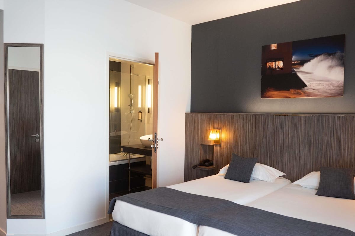 A hotel room with a large bed, a bedside table with a lamp, a mirror, and a painting on the wall.