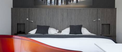 Een moderne hotelkamer met een groot bed, twee nachtkastjes en een wandtelevisie waarop een strand te zien is.