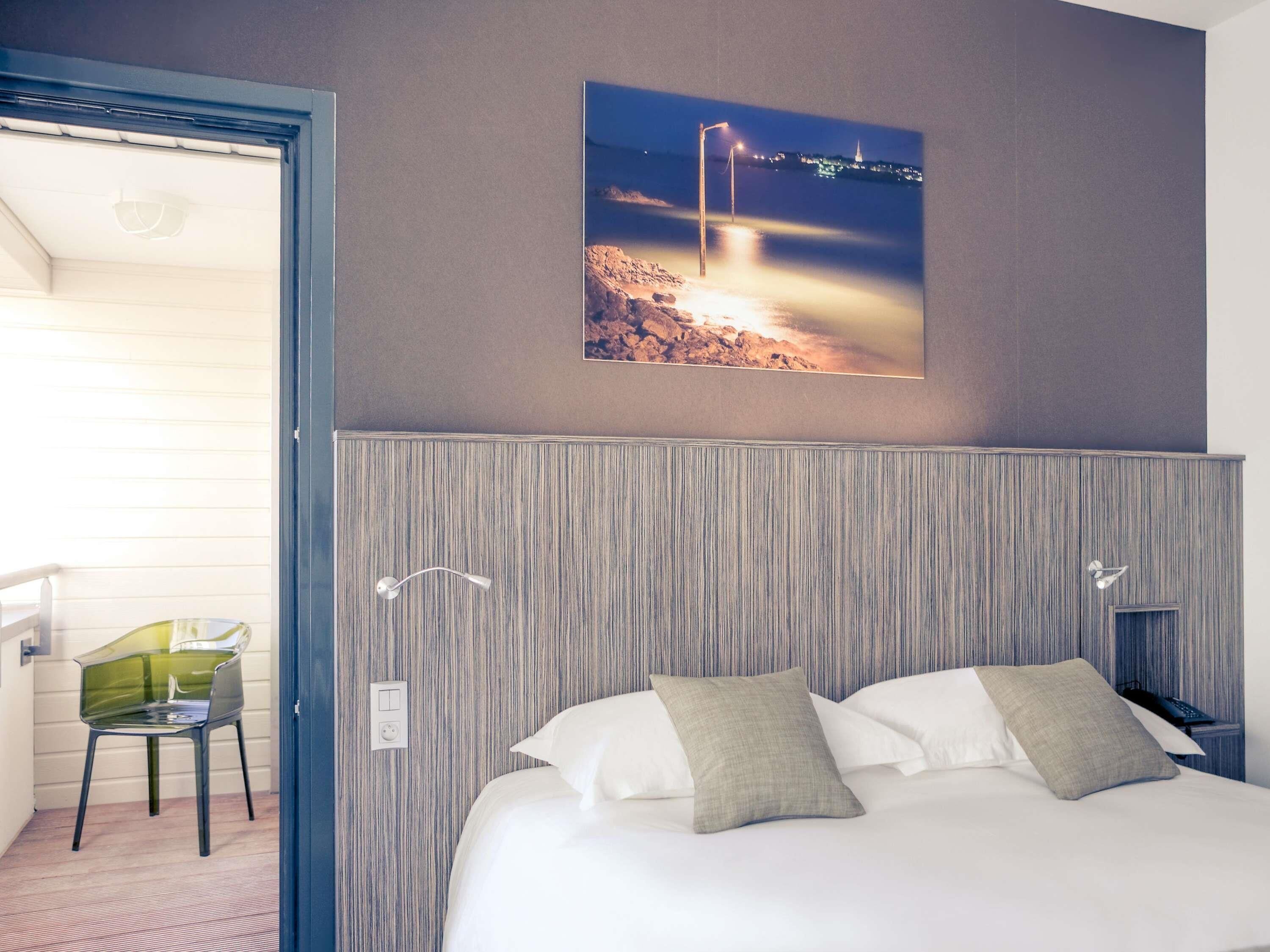 Una habitación de hotel con una cama, una silla, una luz nocturna y un cuadro en la pared.