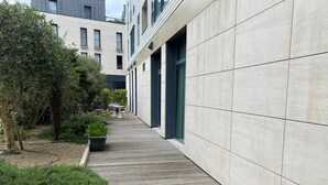 Un bâtiment moderne, à l’allure épurée, avec une façade carrelée et un étroit chemin bordé de verdure et agrémenté de sièges extérieurs.