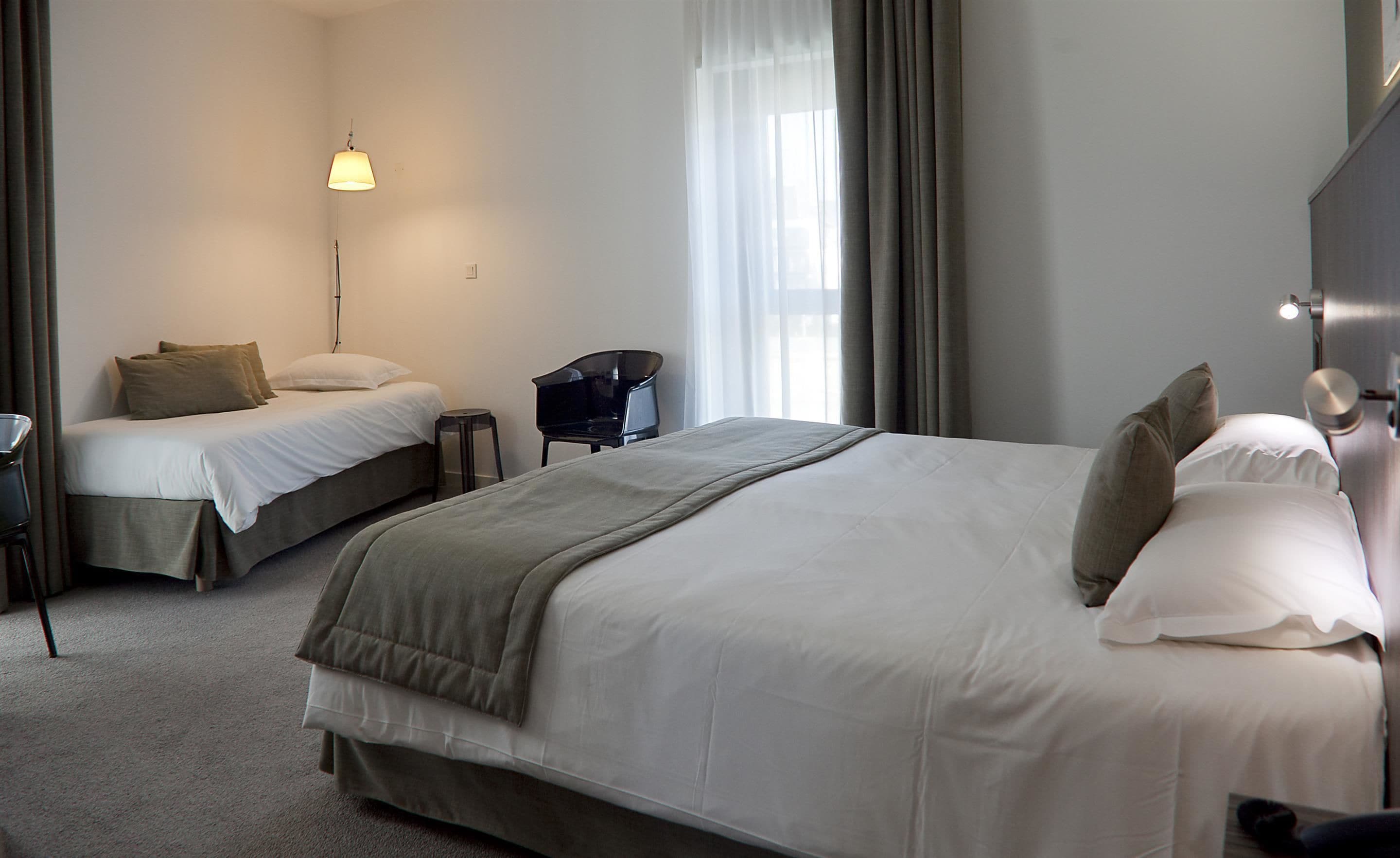 A hotel room with two beds, a desk, a chair, and a lamp.