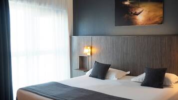 Una habitación de hotel con una cama grande, un cuadro con vistas nocturnas, una lámpara de pared y cortinas de gasa.