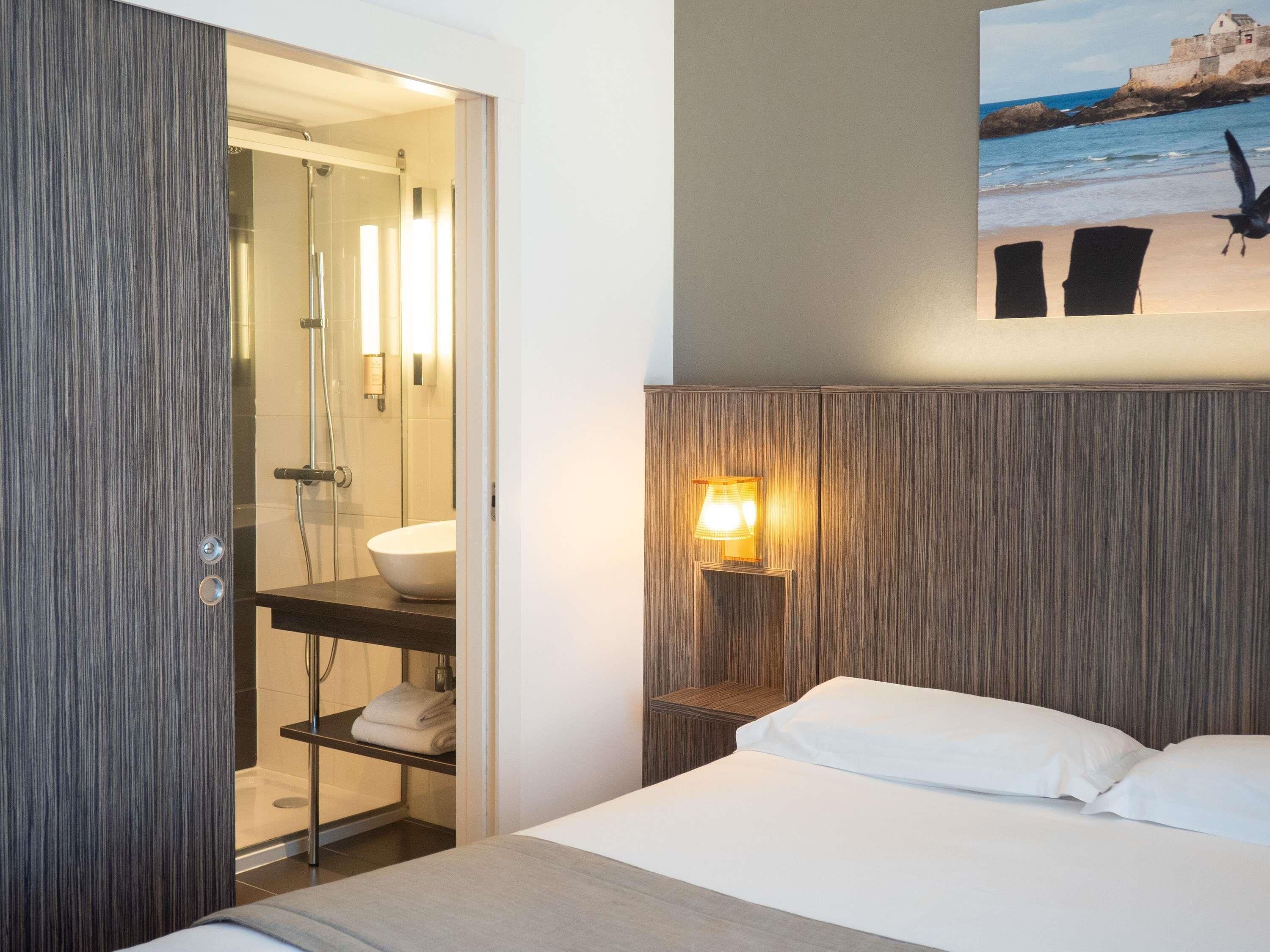 Habitació d'hotel amb un llit, un bany amb dutxa, un lavabo i una làmpada penjada a la paret.