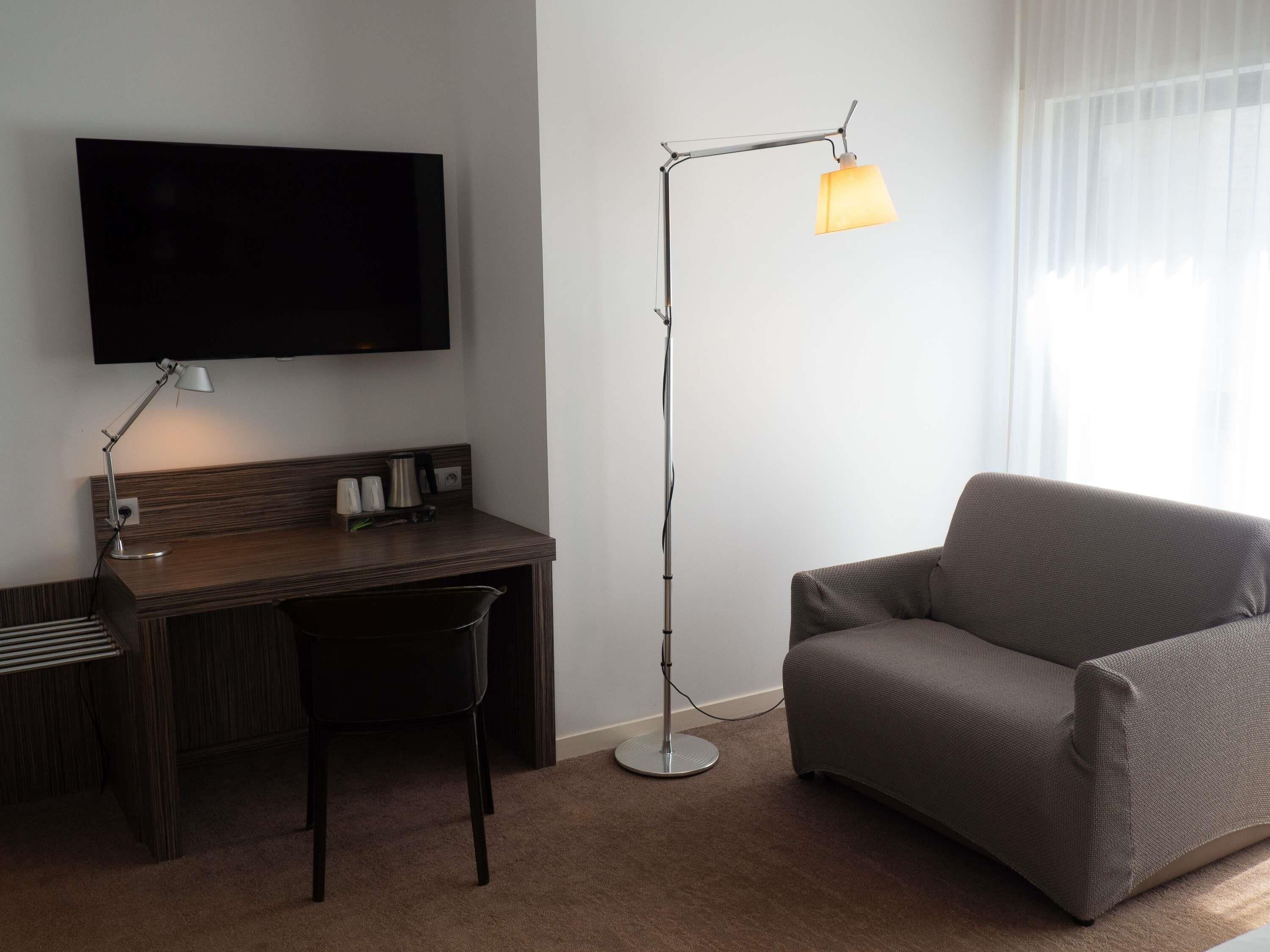 Une chambre d’hôtel équipée d’une télévision à écran plat, d’un bureau avec une chaise, d’une lampe sur pied et d’un canapé.
