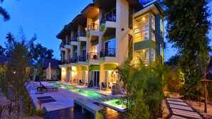 A multi-story hotel with a pool area, outdoor seating, and a well-lit facade. - Panalee Koh Samui Resort (Koh Samui)
