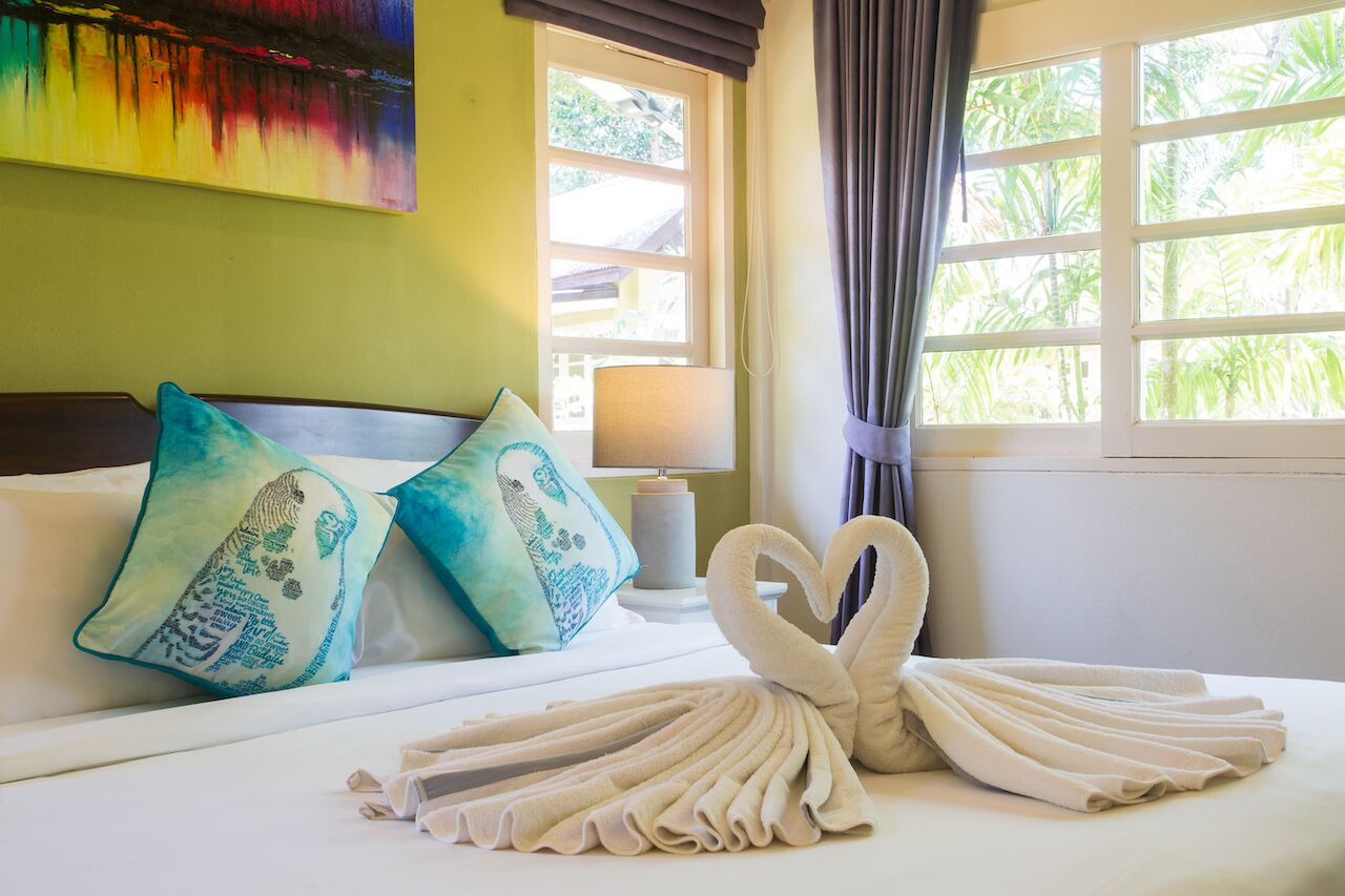 A neatly made bed with decorative pillows, a heart-shaped towel arrangement, and a lamp on a bedside table.