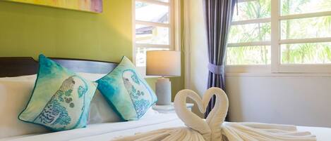 A neatly made bed with decorative pillows, a heart-shaped towel arrangement, and a lamp on a bedside table.
