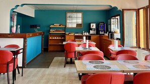 Un restaurante con paredes verde azulado, mesas de madera y sillas rojas. Hay un mostrador con un menú, y una ventana con vistas.