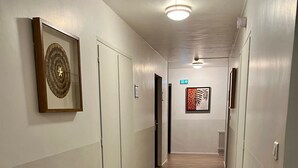 Un pasillo con suelo de madera, paredes blancas y obras de arte enmarcadas. Hay puertas a la izquierda y un radiador a la derecha.