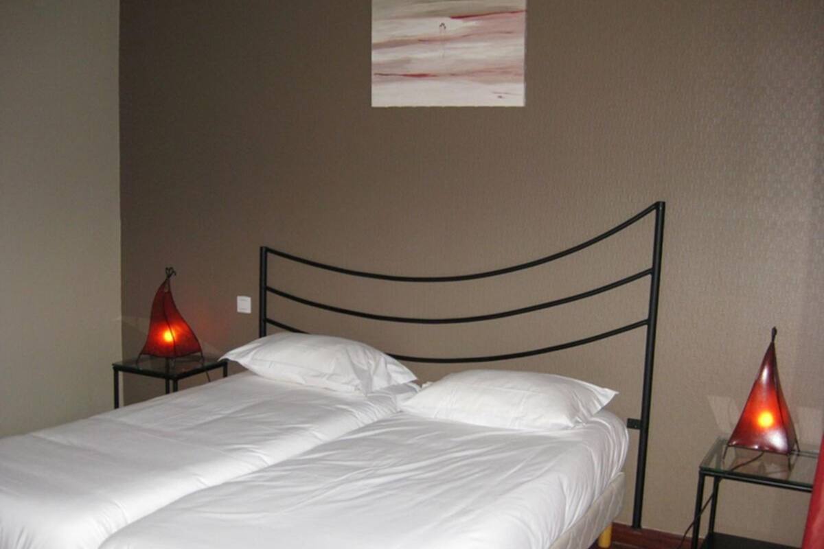 A neatly made bed with white linens in a room with a brown wall and a simple, curved metal headboard.