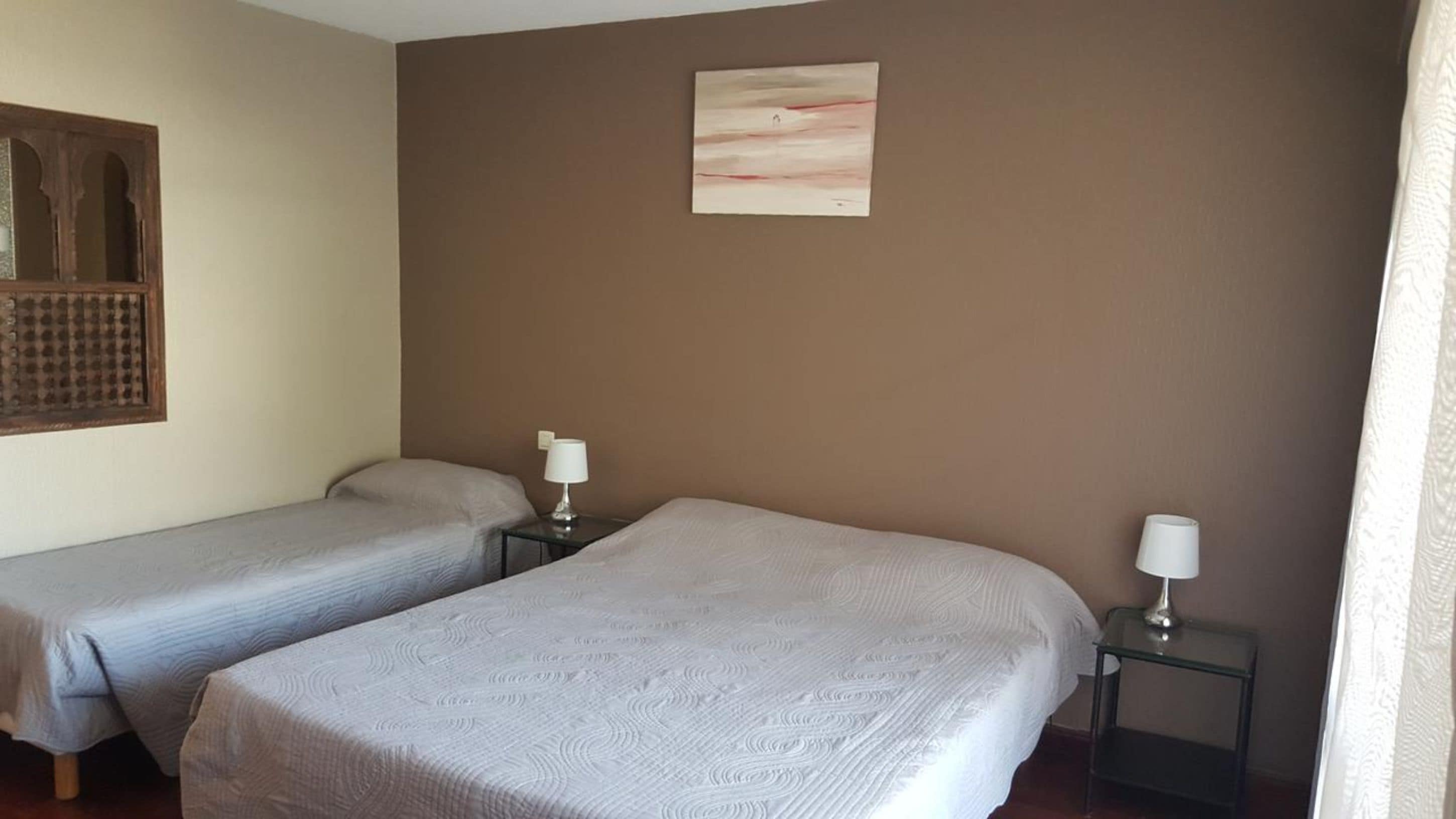 A room with two single beds, each with a bedside table and a lamp.