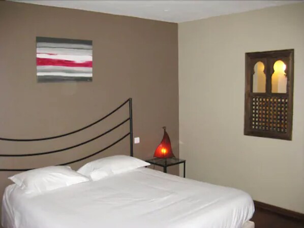 A bedroom with a bed, a wall-mounted artwork, a window with a decorative grille, and a bedside table with a lamp. - Hotel de la Gare (Aix-les-Bains)