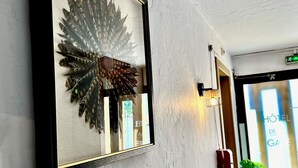 Una obra de arte enmarcada que muestra una estructura emplumada sobre una pared texturizada, una planta en maceta y una puerta con un letrero que dice "Hôtel de GA".