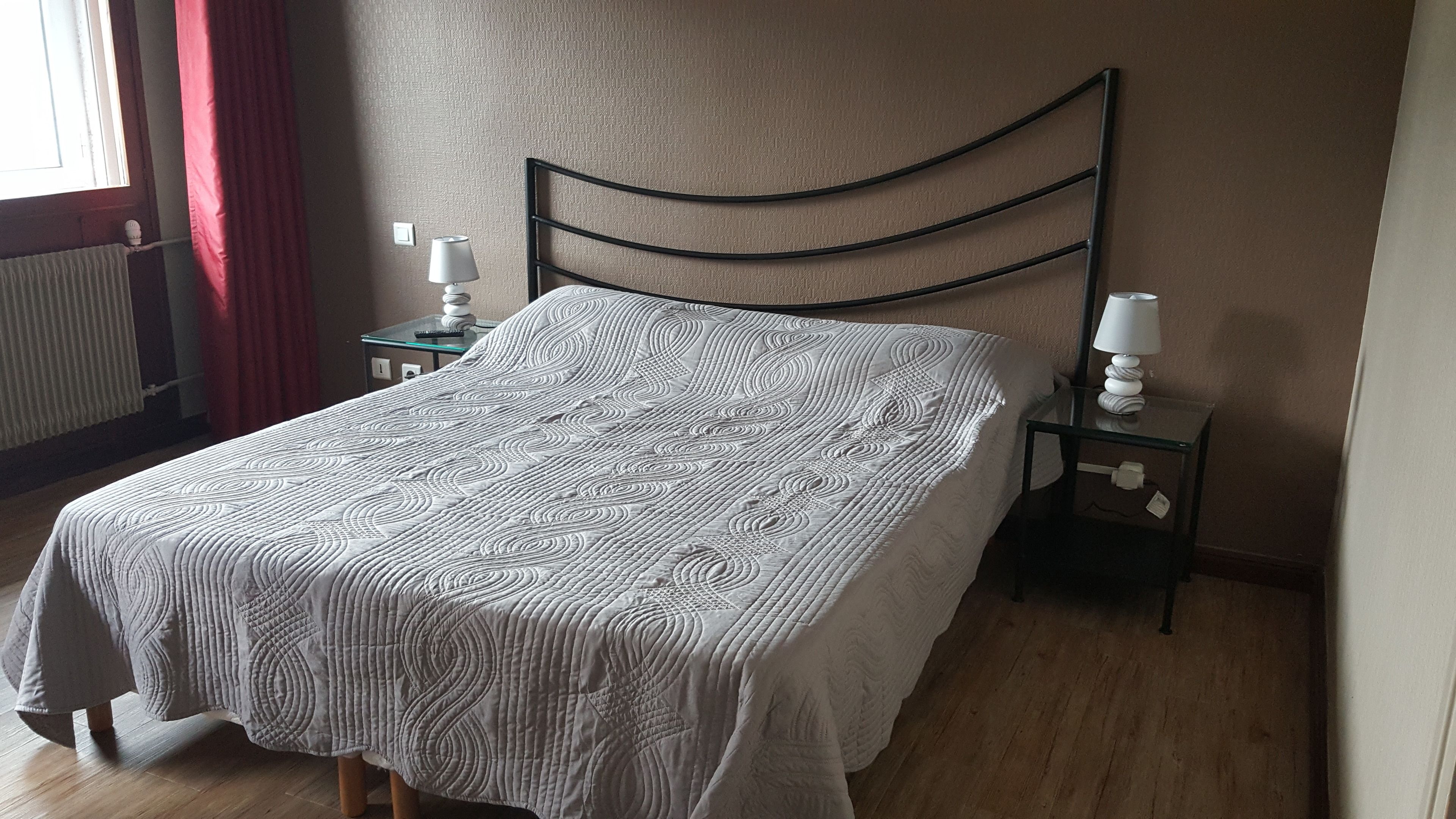 A neatly made bed with a patterned bedspread, a bedside table with a lamp, and a window with curtains.