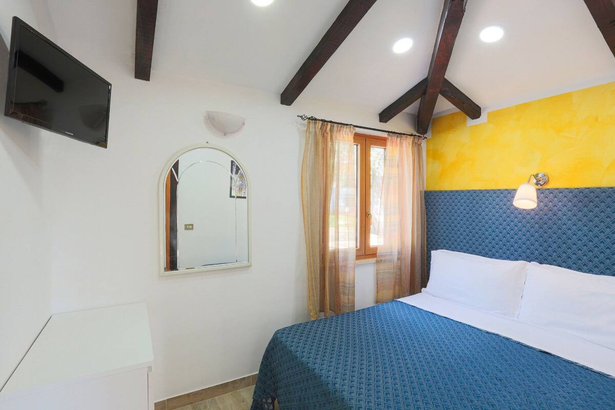 A bedroom with a bed, a mirror, a window with curtains, and a wall-mounted light fixture.
