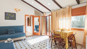 Una habitación con un sofá azul, una mesa de comedor con sillas, una ventana con cortinas y una puerta que da al exterior.